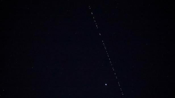 A train of Starlink communications satellites forms a single file of lights crossing the night sky, at Cape Matxitxako