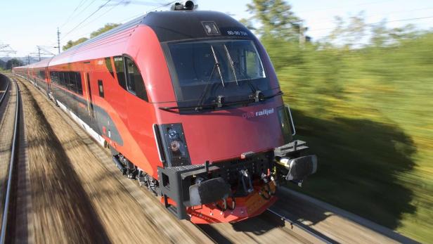 Ein roter ÖBB Railjet-Hochgeschwindigkeitszug fährt auf einer Bahnstrecke.