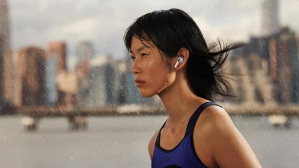 Läuferin trägt Apple AirPods im Regen vor einer Großstadt-Skyline