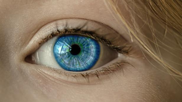 Nahaufnahme eines blauen Auges mit sichtbaren Wimpern und blonden Haarsträhnen am Rand.