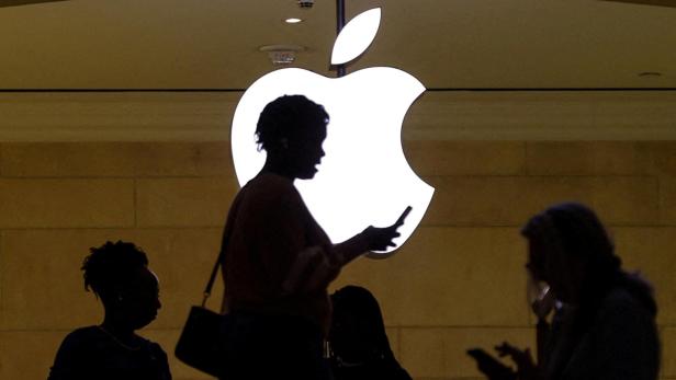 FILE PHOTO: A woman uses her iPhone mobile device as she passes a lighted Apple logo at the Apple store in New York