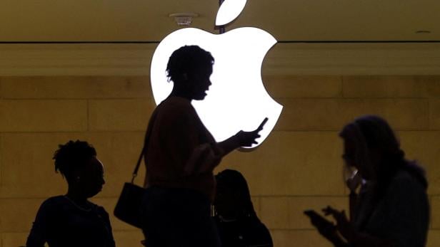 FILE PHOTO: women uses her iPhone mobile device as she passes a lighted Apple logo at the Apple store in New York