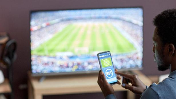 Ein Mann hält ein Smartphone mit einer Sportwetten-App auf dem Bildschirm