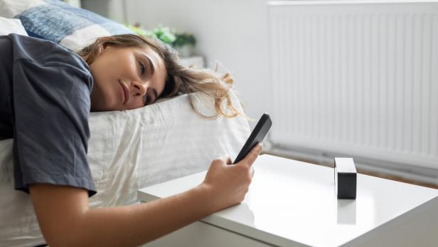 Eine Frau liegt im Bett und hält ein Smartphone in der Hand.