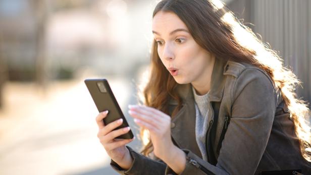 Eine überraschte Frau blickt auf ihr Smartphone.