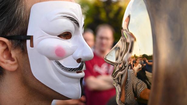 Mann mit Maske vor einer Statue von Satoshi Nakamoto in Budapest