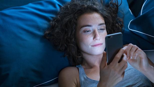 Eine Frau liegt auf einem blauen Kissen und schaut entspannt auf ihr Smartphone.