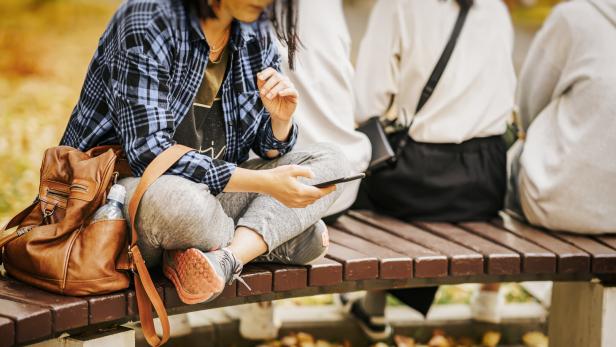 Eine Frau sitzt mit ihrem Smartphone auf einer Bank Eine Frau sitzt mit ihrem Smartphone auf einer Bank