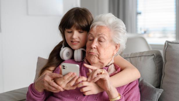 Grandmother with cute girl scrolling on smartphone, girl teaching senior woman to work with technology, internet. Portrait of elderly woman spending time with granddaughter.