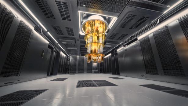 Ein großer, goldfarbener Quantencomputer hängt zentral in einem modernen, technisch ausgestatteten Serverraum von der Decke.