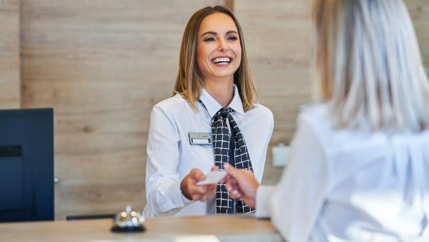 Eine freundliche Rezeptionistin übergibt einem Gast eine Karte.