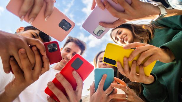 Eine Gruppe junger Leute hält bunte Smartphones in die Höhe.