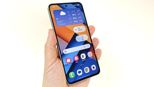 Eine Hand hält ein Smartphone, auf dessen Bildschirm Wetter- und Kalender-Widgets zu sehen sind.