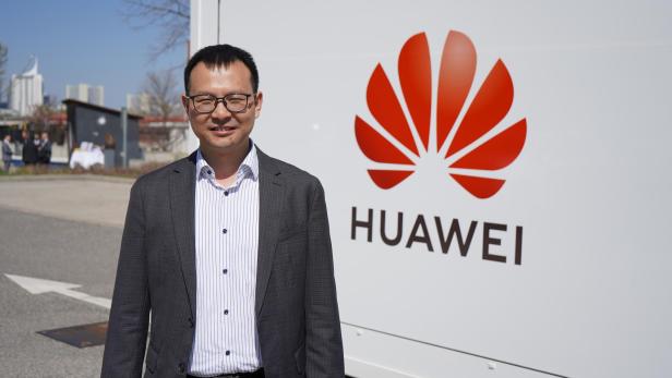 Shane Zhang, Head of Enterprise Business, Huawei Austria Ein asiatischer Mann steht vor dem Logo von HUAWEI.