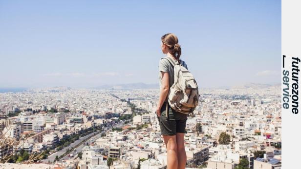 Chatbots helfen bei der Reiseplanung und können auf verschiedene Aspekte Rücksicht nehmen, z.B. Tipps für eine alleinreisende Frau geben (Symbolbild). Eine Frau steht mit Rucksack auf einem Hügel über Athen