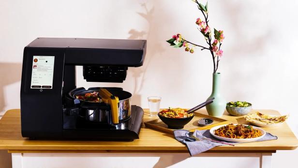 Posha kann Penne all'arrabiata, Ratatouille und asiatische Stir-Frys zubereiten- Posha-Küchengerät auf einem Tisch neben Schüsseln mit Essen
