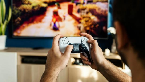 Ein Mann spielt mit einem PlayStation 5-Controller vor einem Fernseher.