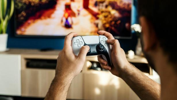 Ein Mann spielt mit einem PlayStation 5-Controller vor einem Fernseher.