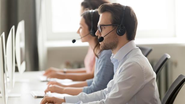 Klarna will wieder Menschen statt KI-Chatbots im Kundenservice einsetzen (Symbolbild). Male call center agent in wireless headset consulting online client