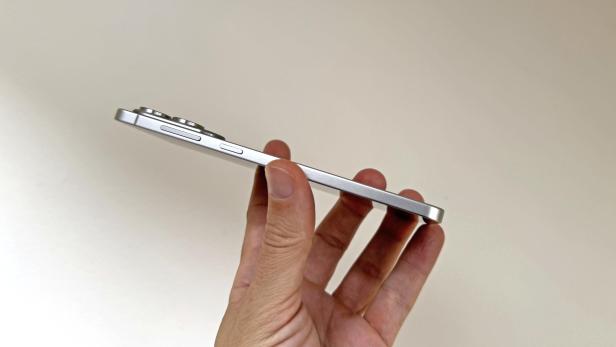 Eine Hand hält ein silbernes Smartphone mit drei Kameralinsen.