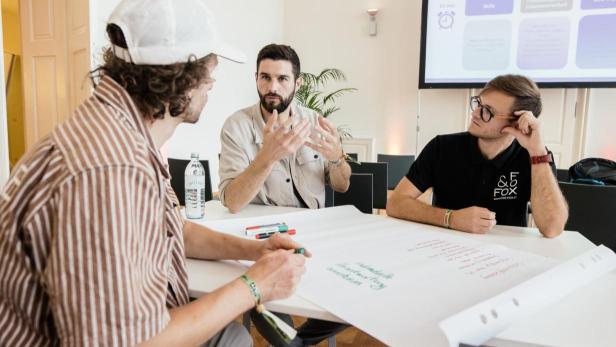 Drei Personen sitzen an einem Tisch während eines Workshops.