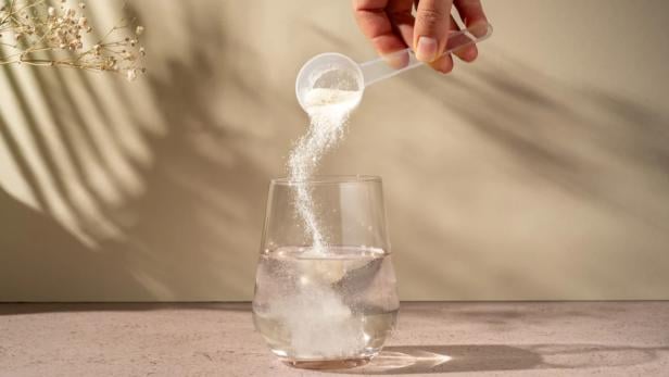 Eine Person kippt einen Löffel mit Basenpulver in ein Glas Wasser zum Auflösen.