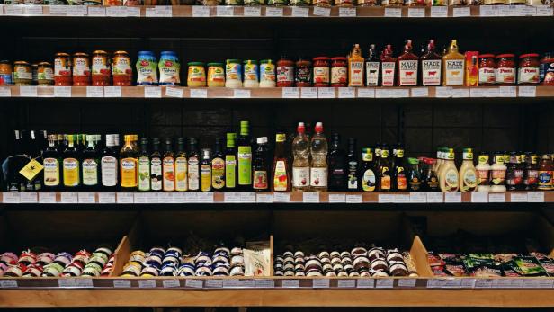 Saucen, Marmeladen und Öle könnten mithilfe der Mikrolaser mit Barcodes versehen werden (Symbolbild). ein Supermarktregal mit Konserven in Gläsern und Olivenöl