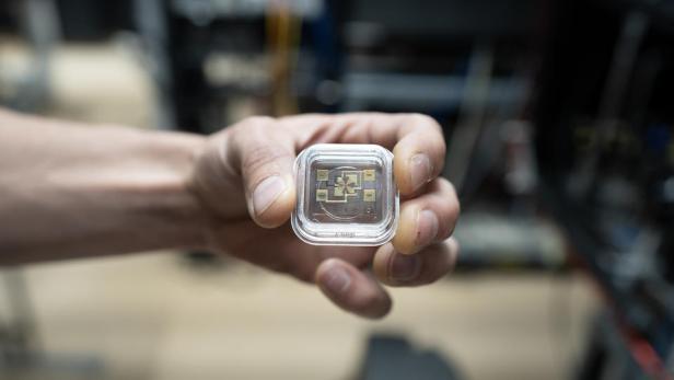 Die neue Ionen-Falle der NIST-Atomuhr ist für Aluminium- und Magnesium-Ionen gedacht. Eine Hand hält eine transparente Box, die mehrere goldene Rechtecke enthält