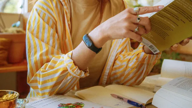 Eine Person liest ein Buch am Tisch, auf dem weitere Bücher und ein Stift liegen.