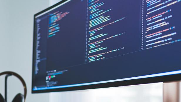 Ein Schreibtisch mit einem Computerbildschirm, der Codes anzeigt.