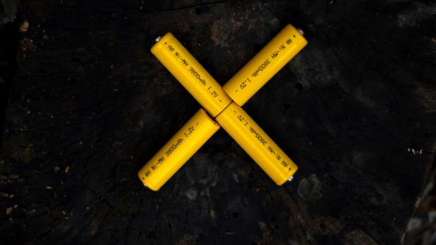 Gelbe AA-Batterien liegen kreuzförmig auf einem Baumstumpf.