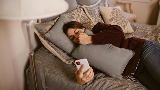 Eine Frau liegt auf einem Bett und schaut auf ihr Smartphone