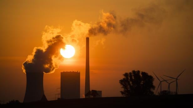Ein Kohlekraftwerk und Windräder im goldenen Abendlicht.