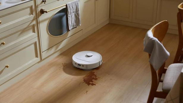 Ein Roboterstaubsauger wischt eine Flüssigkeit auf einem Holzboden auf.