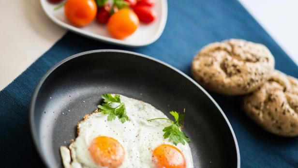 Spiegeleier in einer Bratpfanne, serviert mit Brötchen und Tomaten.