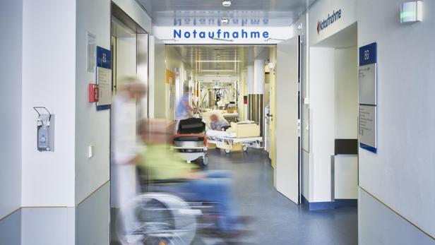 Ein Patient wird im Rollstuhl durch den Flur der Notaufnahme eines Krankenhauses gefahren.