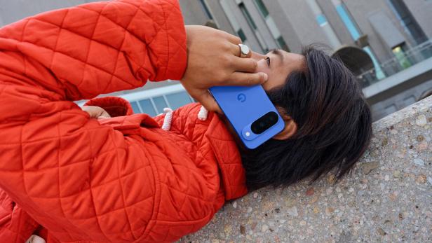 Eine Person in einer roten Jacke telefoniert mit einem blauen Google Pixel Handy.