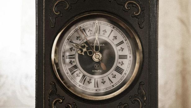 Eine alte, dekorative Tischuhr mit römischen Ziffern steht auf einem Tisch.