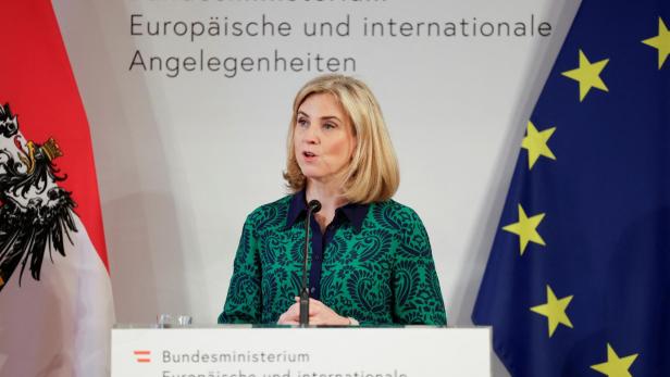 Eine Frau spricht vor Flaggen des Außenministeriums und der EU.