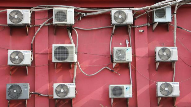 Mehrere Klimaanlagen verschiedener Hersteller hängen an einer roten Wand.