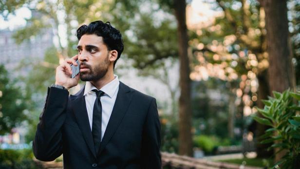 Anzugträger mit Smartphone am Ohr schaut skeptisch.