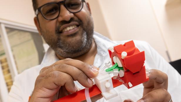 Ein Mann untersucht ein rot-weißes Modell eines „Augen-ECMOs“.