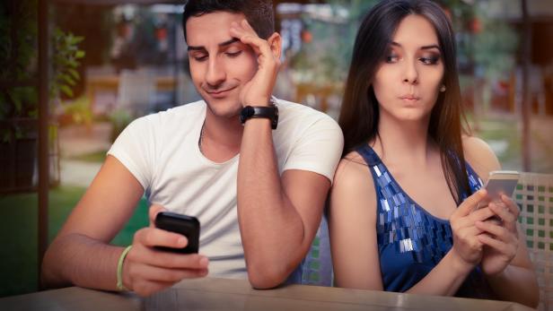 Symbolbild: Eine Frau liest am Smartphone eines Mannes Nachrichten mit.