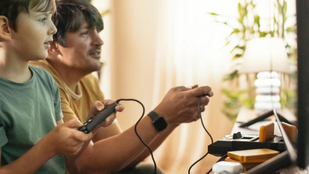 Vater und Sohn spielen auf einer alten Videospielkonsole.