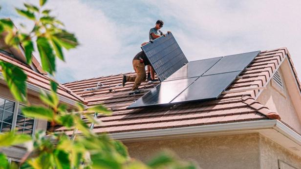 Zwei Arbeiter installieren Solarmodule auf einem Hausdach.