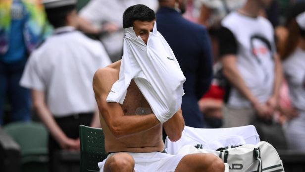 Novak Djokovic zieht sich ein weißes Shirt an.
