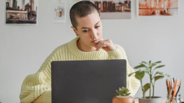 Eine Person sitzt nachdenklich vor einem Laptop an einem Schreibtisch.