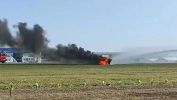 Ein brennendes Fahrzeug steht auf einer Wiese.