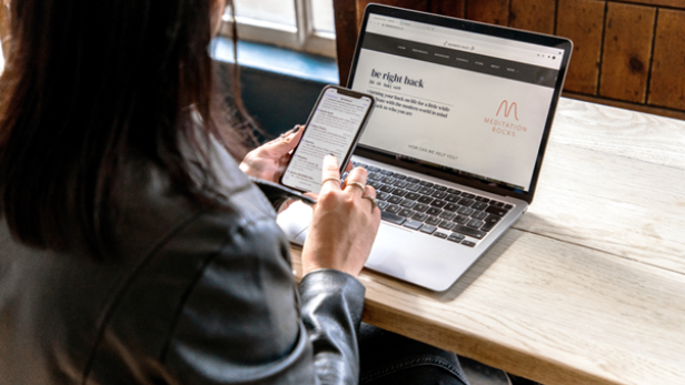 Eine Frau sitzt an einem Laptop und ist an ihrem Handy.