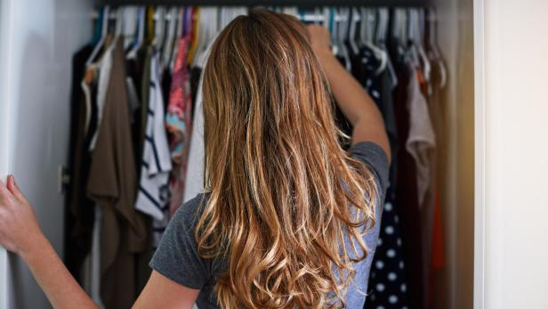 Eine Frau schaut in ihren Kleiderschrank, man sieht die Szene von hinten.